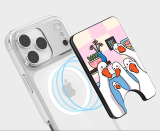 A clear MagSafe-compatible phone case with a built-in magnetic stand, shown alongside a phone and an illustration of three penguins on a pink and cream checkered background. Text at the top reads 'MAGSAFE COMPATIBLE' with a small magnet icon.